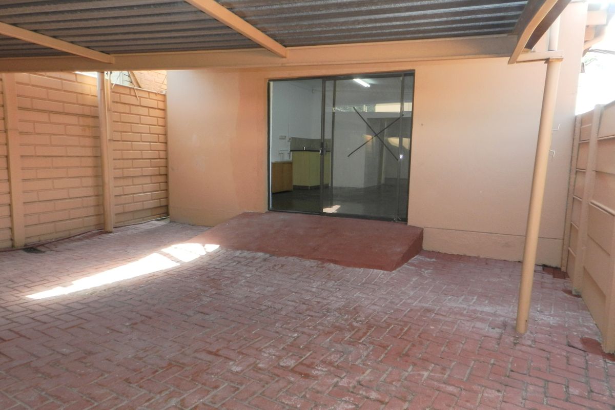A covered rear patio area featuring paved flooring, a sliding glass door entrance, and enclosed by brick boundary walls.