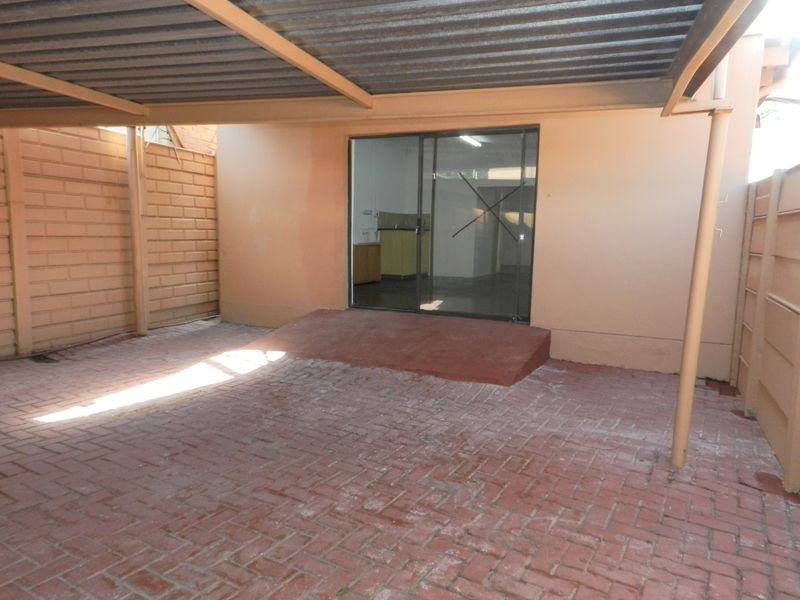 A covered rear patio area featuring paved flooring, a sliding glass door entrance, and enclosed by brick boundary walls.