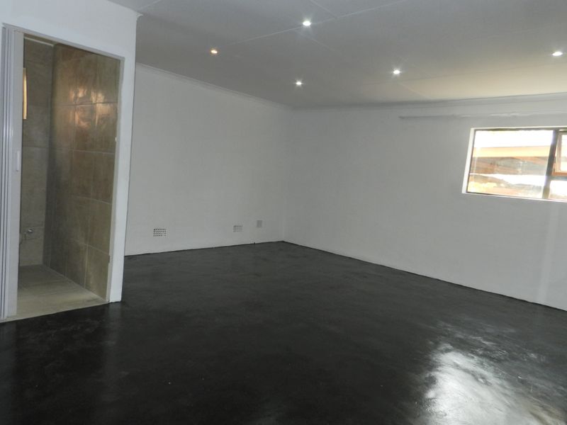 An empty bedroom featuring painted concrete floors, recessed downlighting, and an adjoining tiled ensuite bathroom.