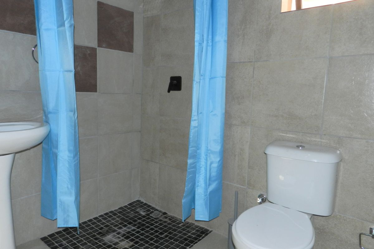 A functional bathroom featuring a pedestal basin, toilet, and a tiled shower area with wall-mounted mixer.