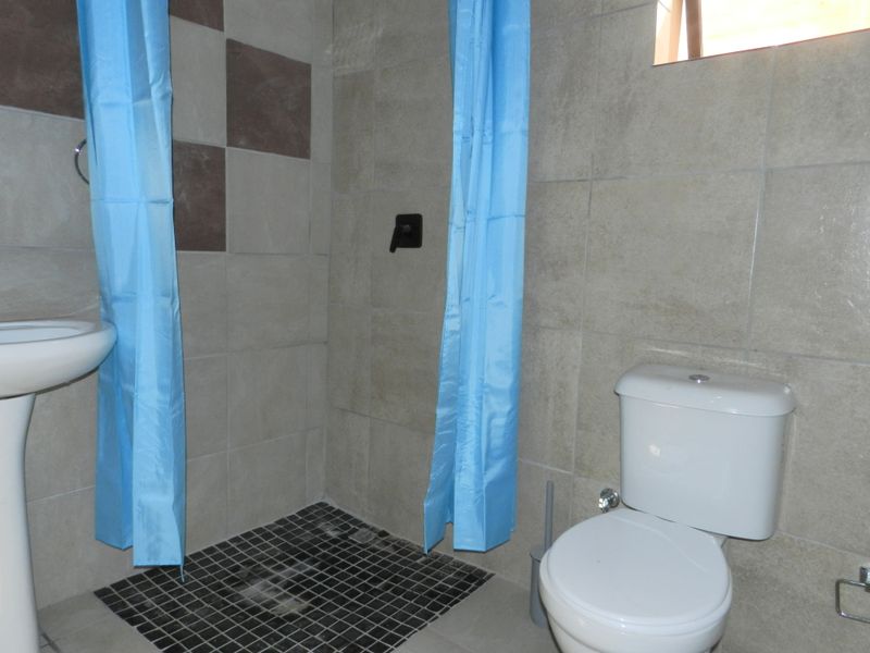 A functional bathroom featuring a pedestal basin, toilet, and a tiled shower area with wall-mounted mixer.