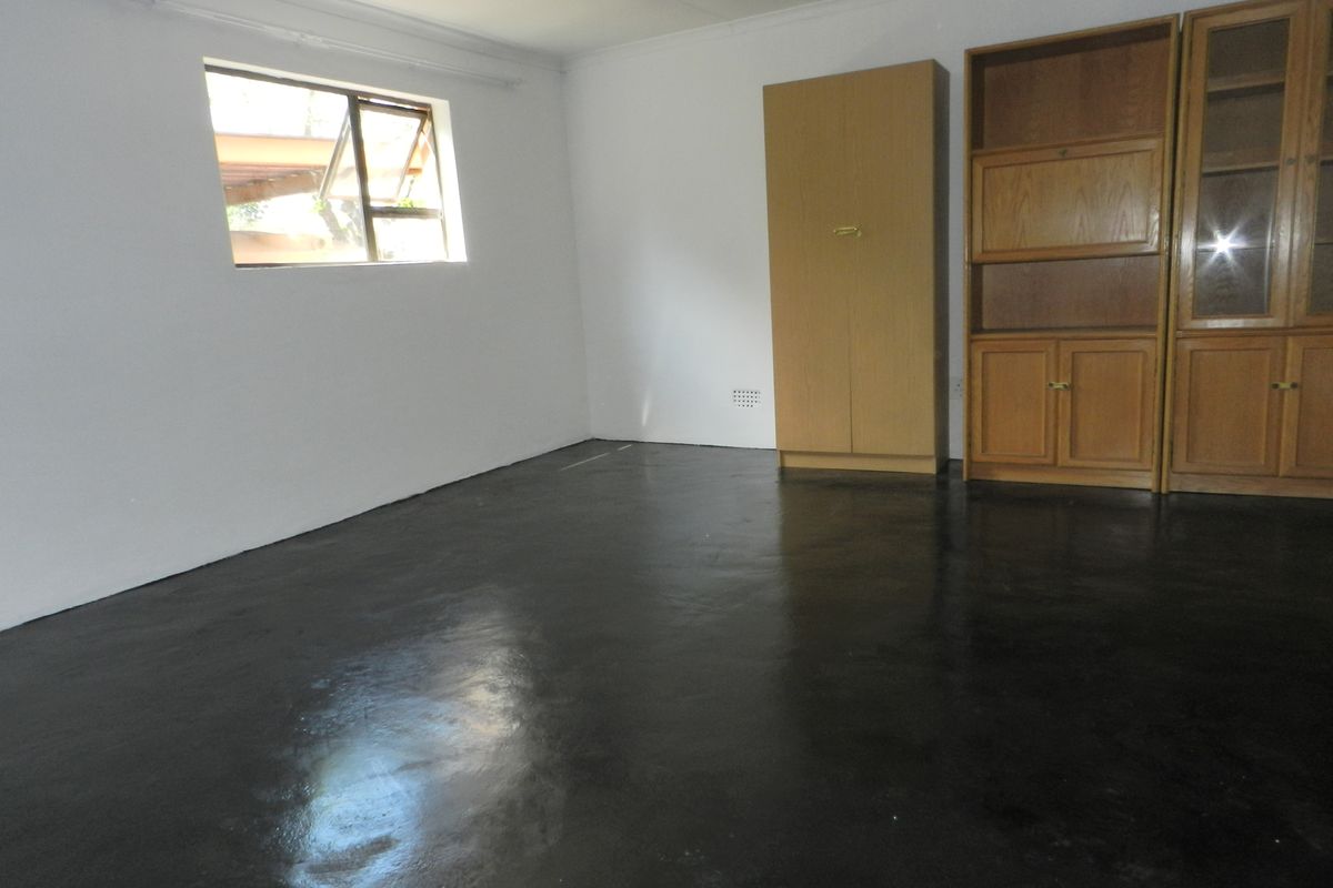 A bedroom featuring painted concrete flooring, built-in wooden cabinetry, and a casement window, offering a blank canvas for potential interior updates.