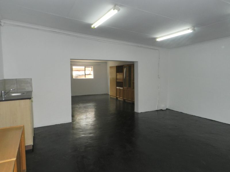 An open-plan living and kitchen area featuring painted concrete floors, basic cabinetry, and functional fluorescent lighting, offering a blank canvas for renovation.