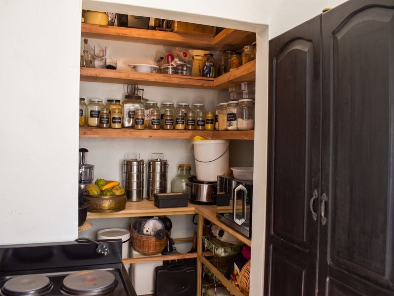A functional walk-in pantry or scullery area featuring extensive built-in wooden shelving for organized storage and adjacent dark cabinetry.