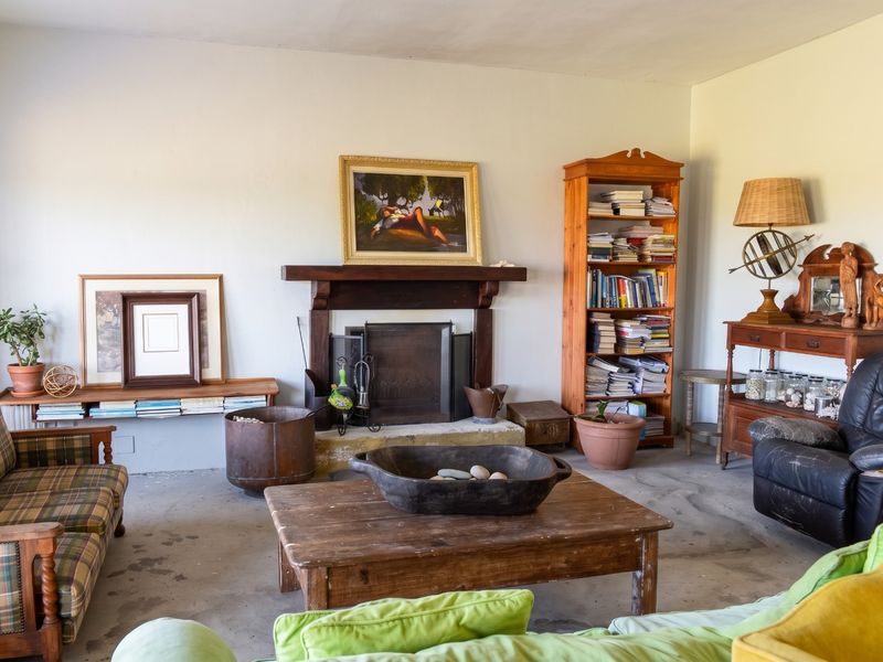 A living room featuring a traditional fireplace with a wooden mantelpiece and exposed concrete flooring, offering a rustic foundation for potential renovation.