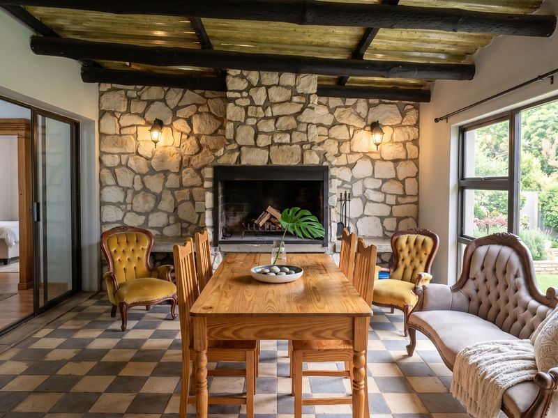 A charming enclosed patio featuring a rustic stone fireplace, exposed timber beams, and classic checkered tile flooring, offering a cozy space for dining.