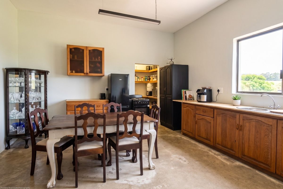 A functional kitchen featuring wooden cabinetry, a stainless steel sink, and an adjoining pantry, with a dining area and concrete flooring.