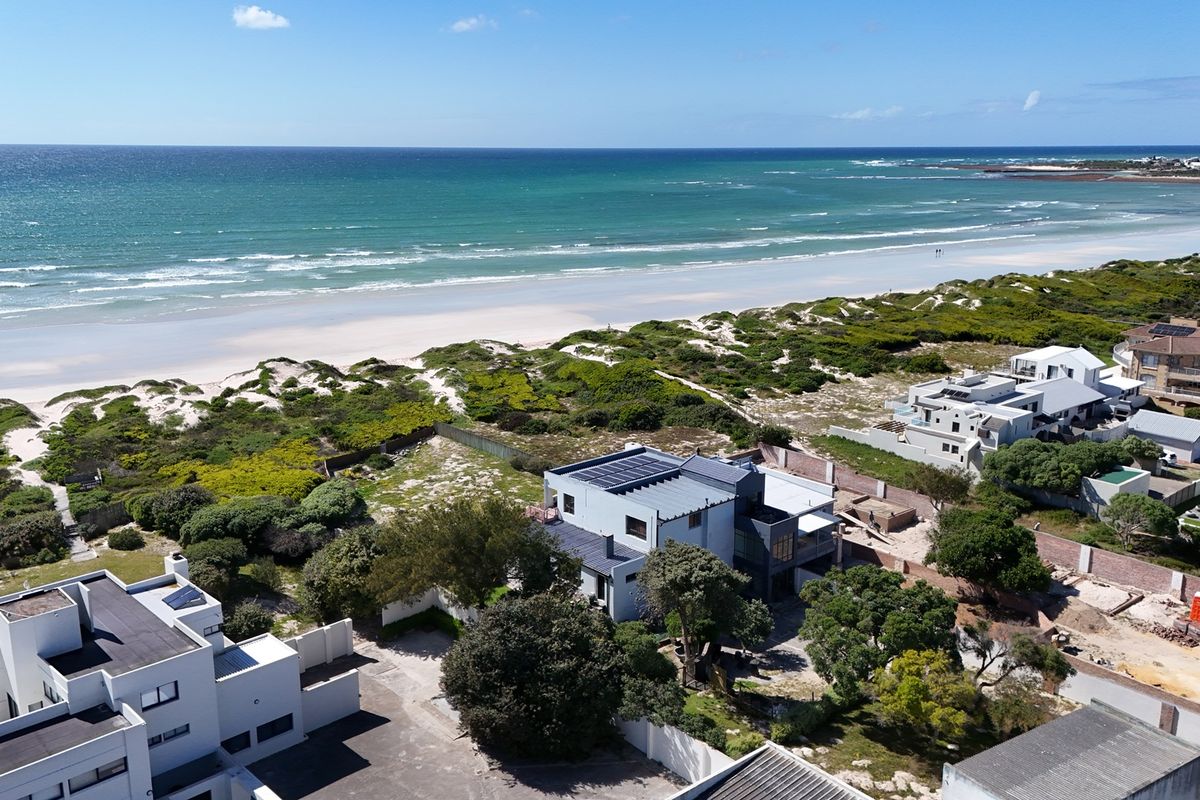 Aerial view of a coastal property featuring solar panels, boundary walls, and proximity to the beach and ocean.