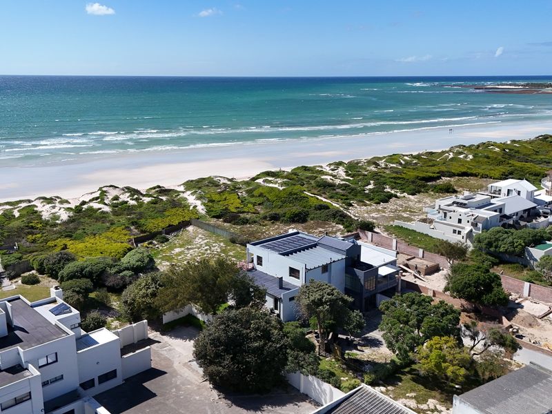 Aerial view of a coastal property featuring solar panels, boundary walls, and proximity to the beach and ocean.