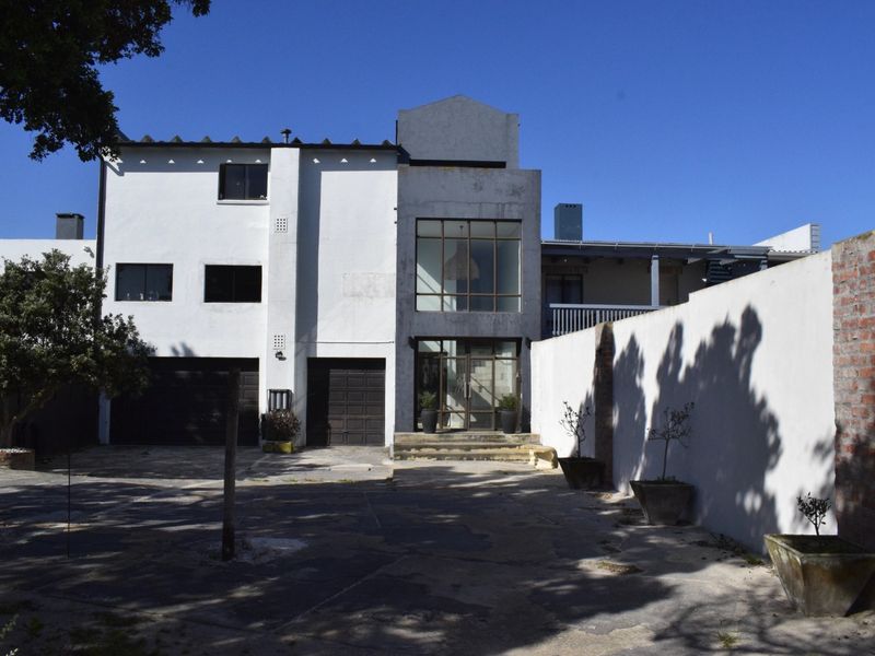 Front elevation of a multi-level residence featuring a double garage, large glass entrance facade, and a paved driveway with a boundary wall.