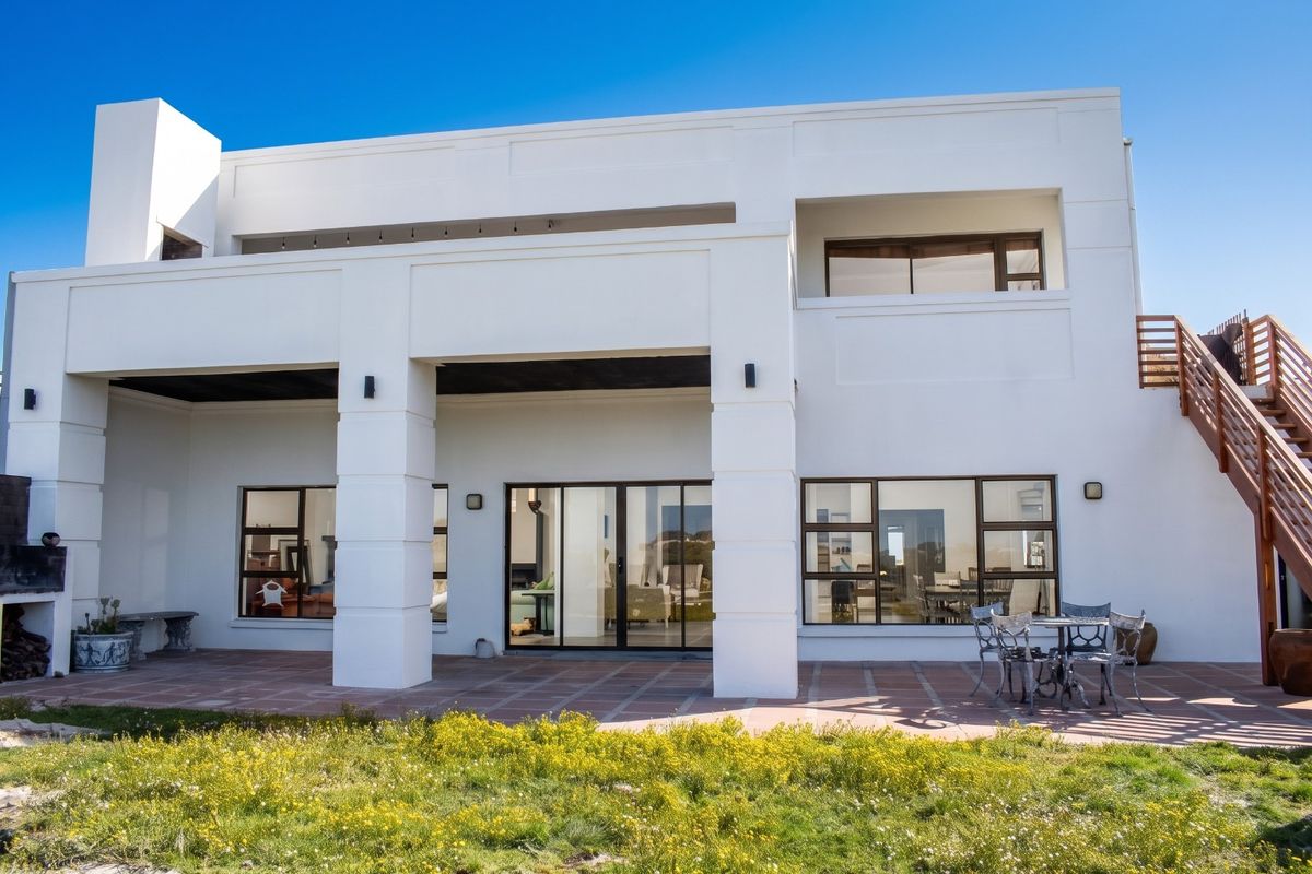Rear view of a modern two-story house featuring a spacious tiled patio, built-in outdoor fireplace, and an external staircase leading to the upper level.