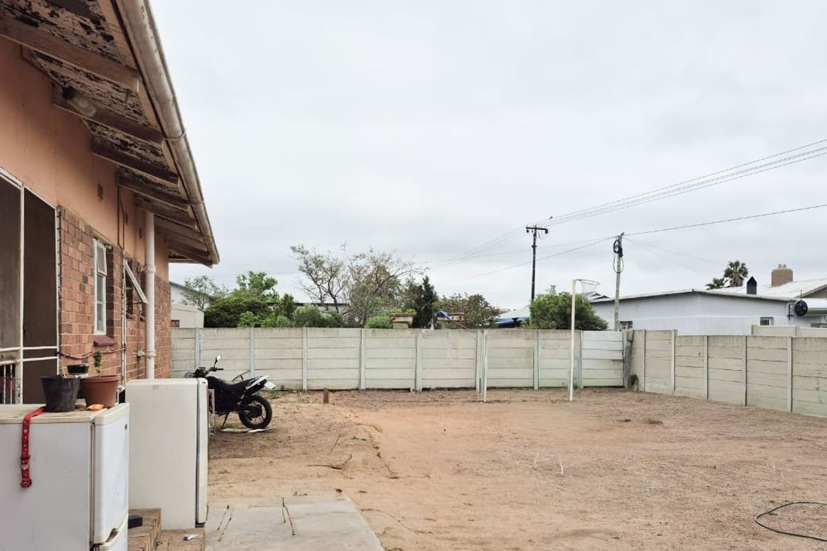 Rear exterior view of the property featuring a large open yard area enclosed by a precast concrete boundary wall and brick building facade.