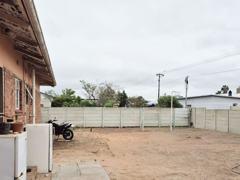 Rear exterior view of the property featuring a large open yard area enclosed by a precast concrete boundary wall and brick building facade.