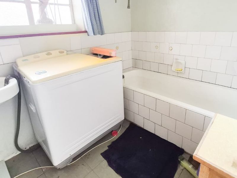 A functional bathroom featuring a bathtub, wall-mounted basin, and tiled splashback, offering potential for modernization and cosmetic updates.