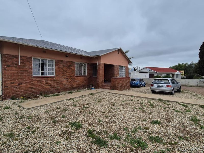 Front view of a single-story brick house featuring a corrugated metal roof, concrete walkway, and a gravel driveway area.