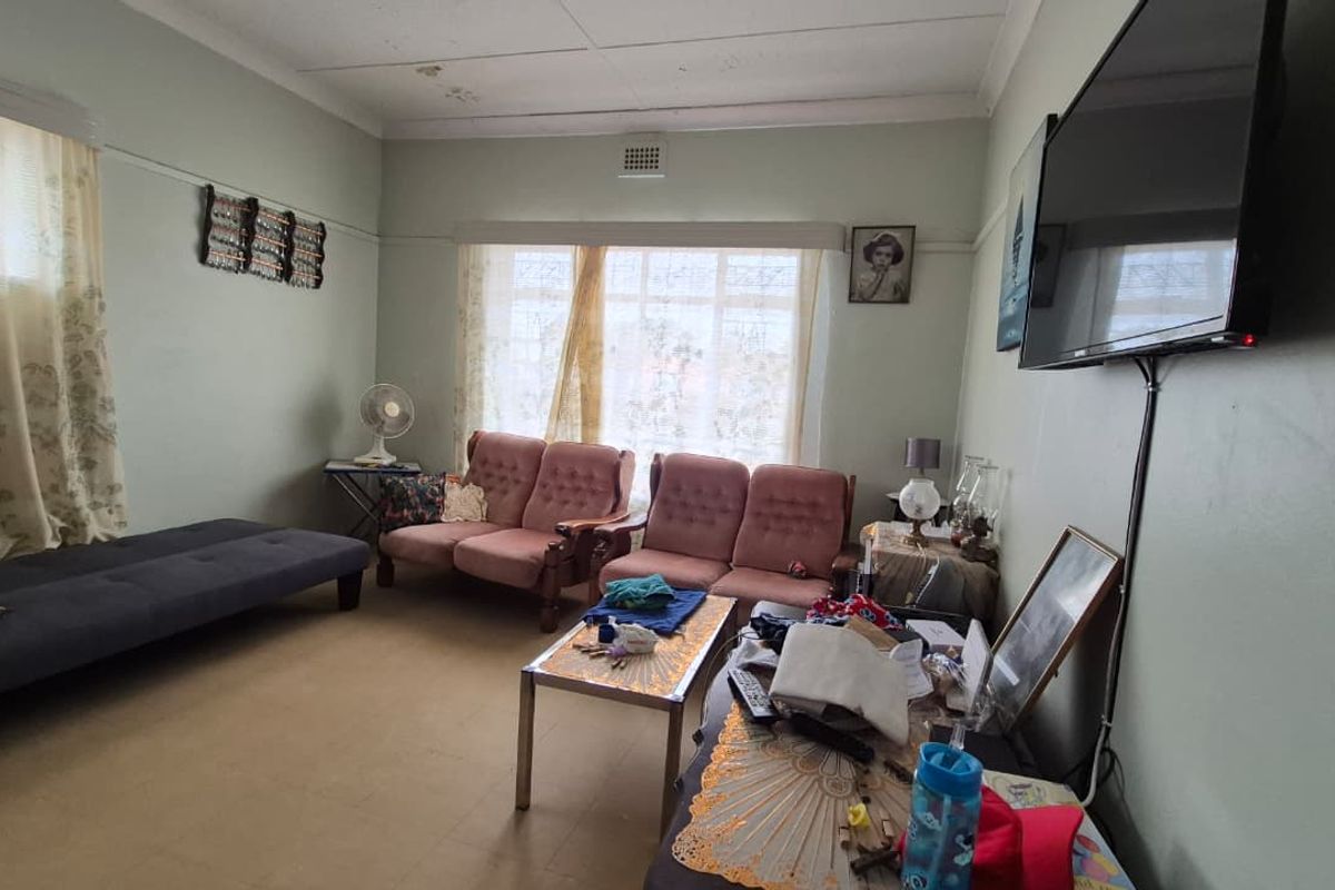 A living room featuring a coved ceiling and ventilation grille, currently showing signs of wear on the flooring and ceiling.