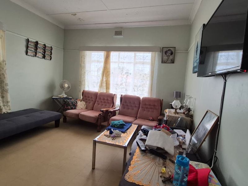 A living room featuring a coved ceiling and ventilation grille, currently showing signs of wear on the flooring and ceiling.