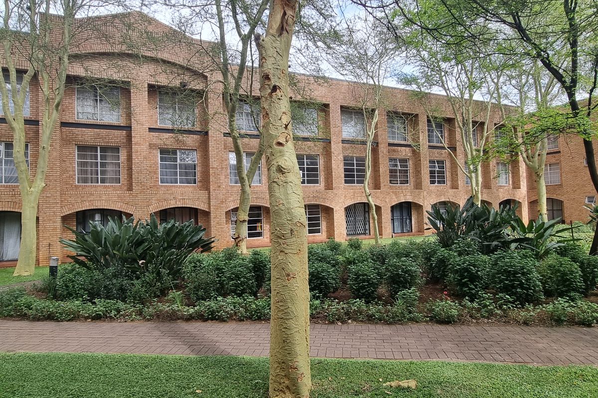 A view of the rear brick facade of the flat complex, featuring a well-maintained garden and paved walkway.