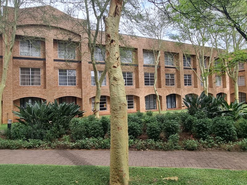 A view of the rear brick facade of the flat complex, featuring a well-maintained garden and paved walkway.