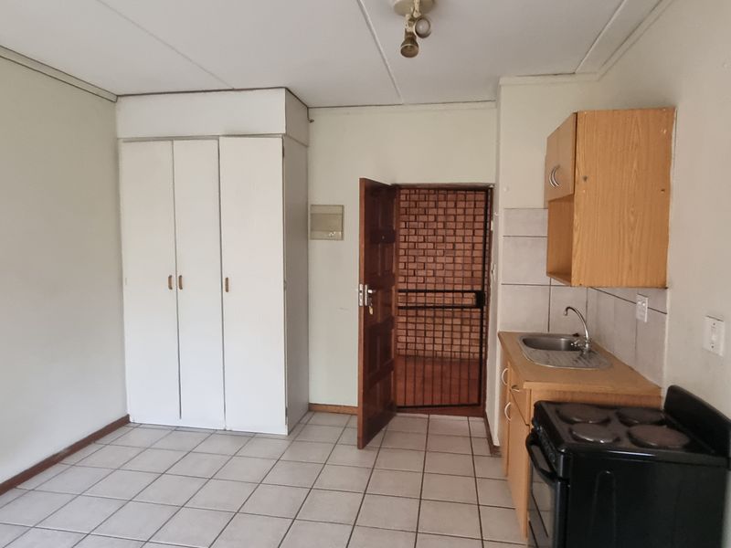 Open plan living area featuring tiled flooring, built-in cupboards, and a compact kitchenette with basic cabinetry and an electric stove.