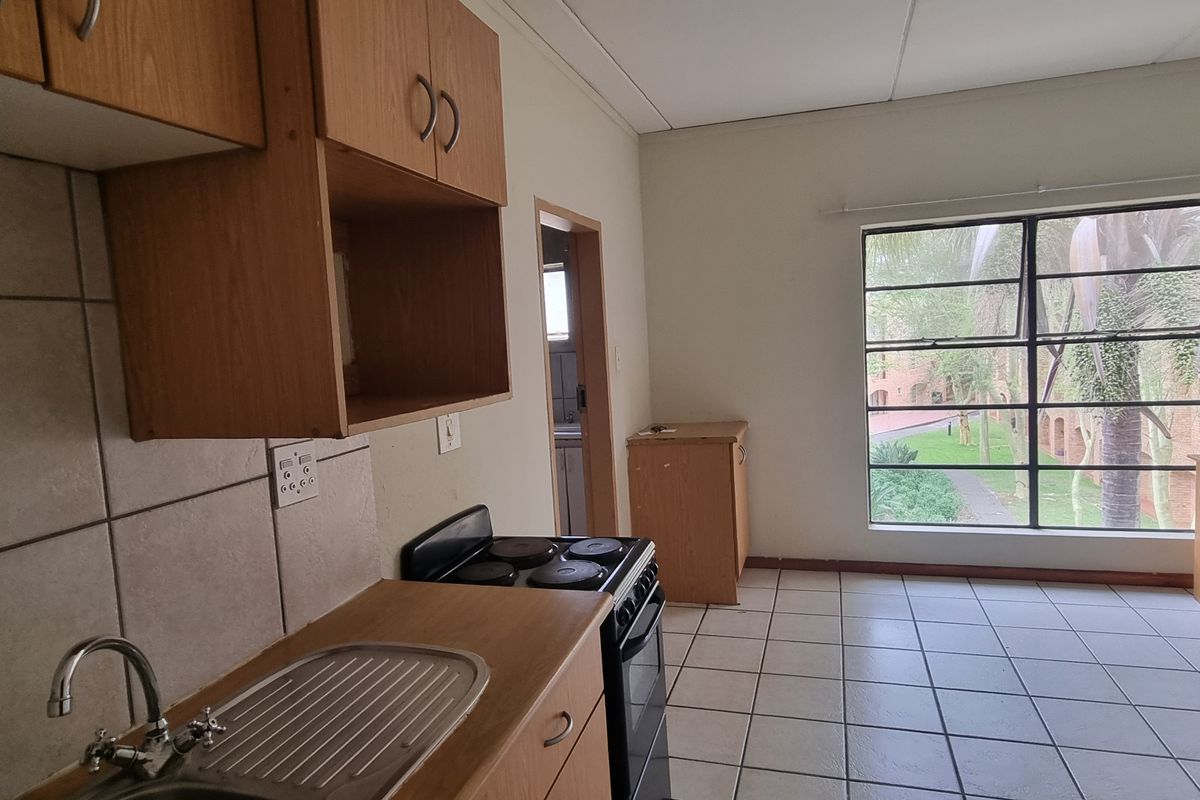 Open plan kitchen and living area featuring tiled flooring, built-in cabinetry, and a large window providing natural light and garden views.