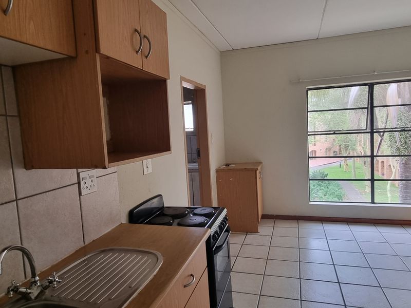 Open plan kitchen and living area featuring tiled flooring, built-in cabinetry, and a large window providing natural light and garden views.