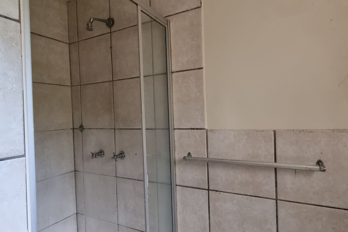 A bathroom shower area featuring tiled walls, a glass shower enclosure, and a wall-mounted towel rail, currently showing signs of wear.