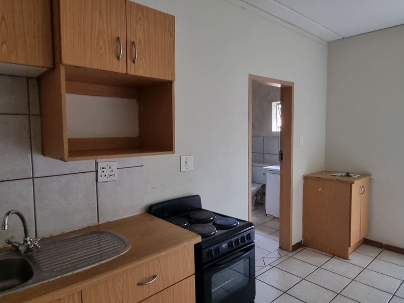 A functional kitchen featuring wooden cabinetry, a stainless steel sink, tiled backsplash, and a freestanding stove, with direct access to an adjacent room.