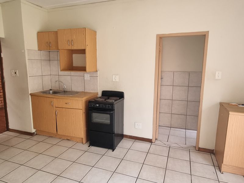 A functional kitchen area featuring tiled flooring, basic cabinetry, a stainless steel sink, and a freestanding stove, offering potential for modernization.