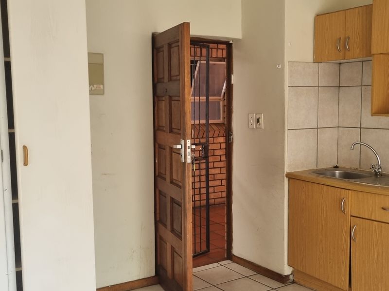 A compact kitchen featuring wooden cabinetry, a stainless steel sink, tiled backsplash, and a built-in oven, with direct access to an exterior area.