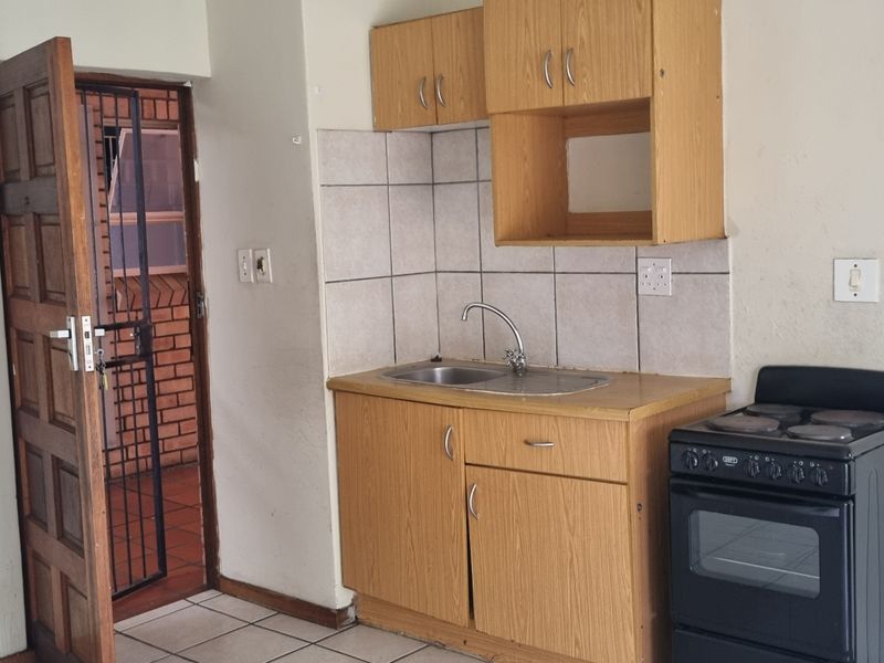 A compact kitchen featuring laminate cabinetry, a stainless steel sink, tiled splashback, and a freestanding stove, with direct access to an external security gate.