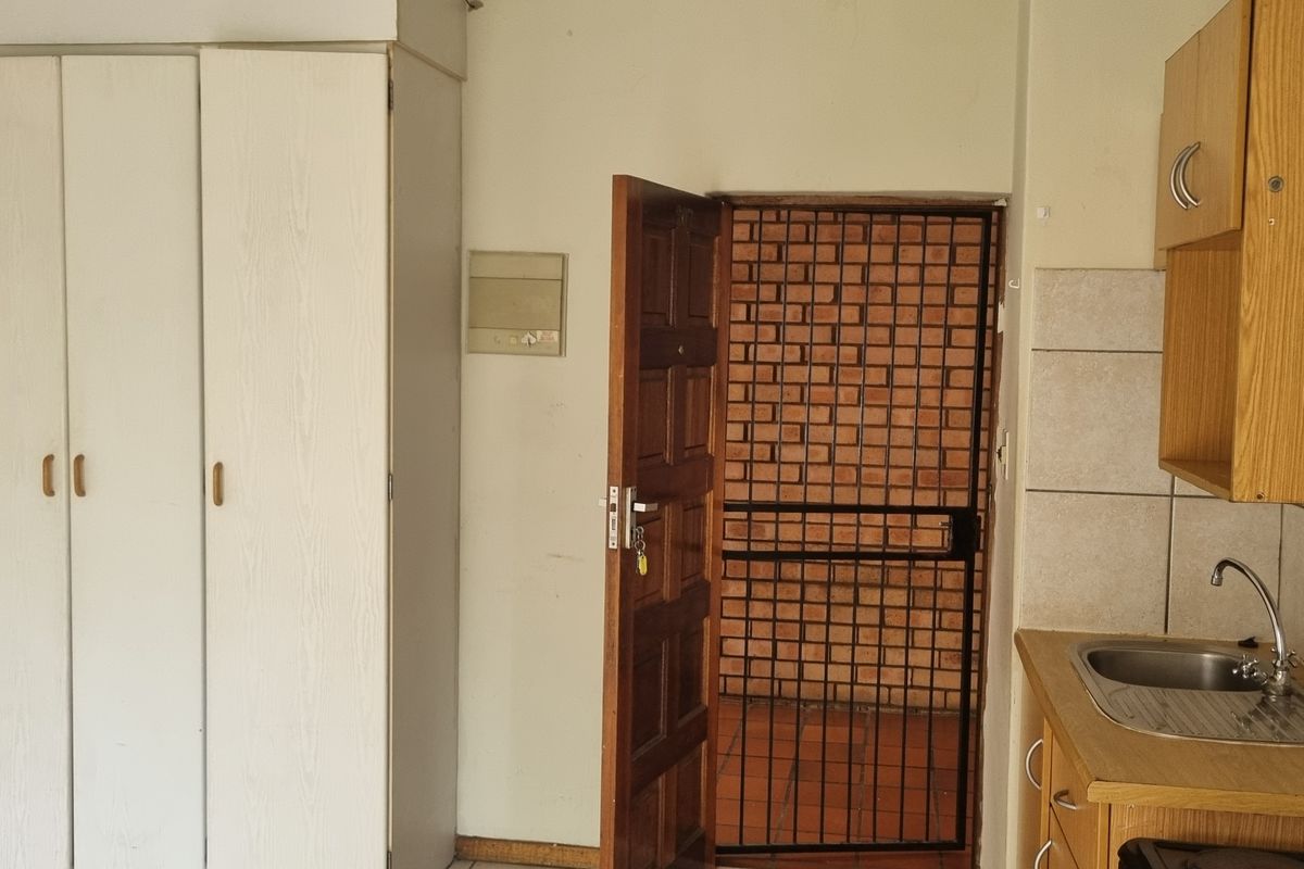 A compact kitchen area featuring built-in cabinetry, a stainless steel sink, and direct access to an exterior security gate.