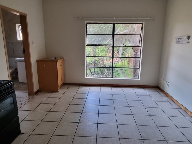 An open-plan living and kitchen area featuring tiled flooring, wooden cabinetry, and a large window with garden views.