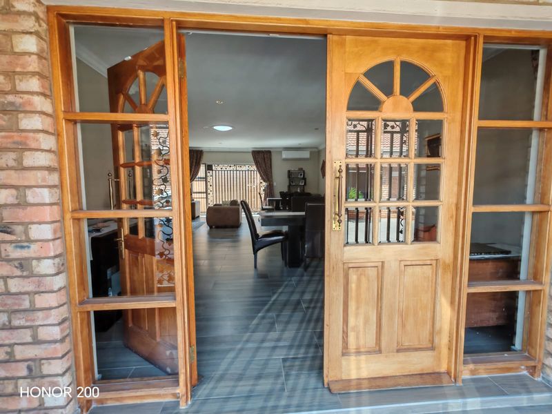 Entrance view through timber framed glass doors into an open plan living and dining area featuring tiled flooring and modern recessed lighting.