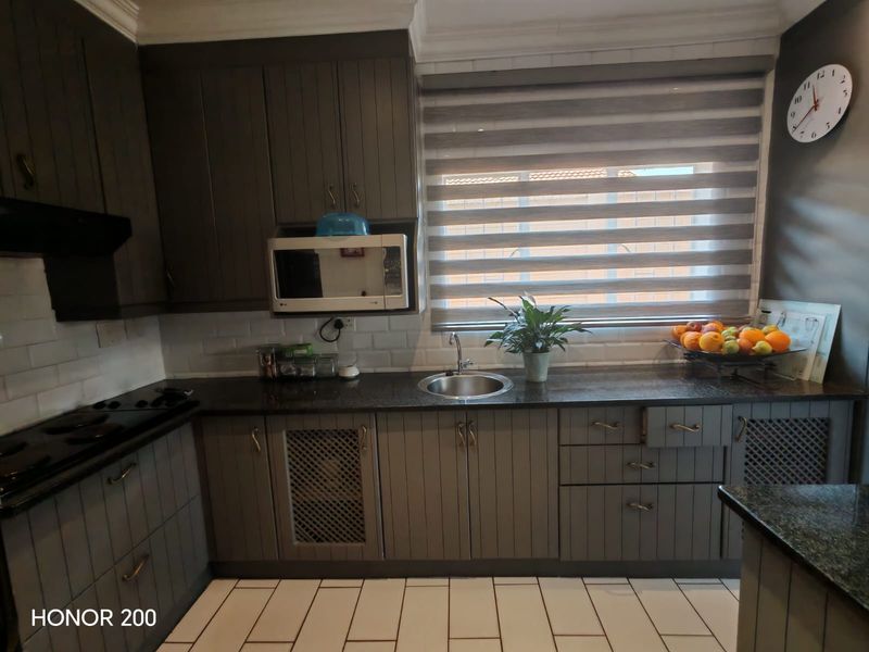 A well-maintained kitchen featuring dark grey cabinetry, granite countertops, subway tile backsplash, and integrated appliances, offering a functional and modern cooking space.