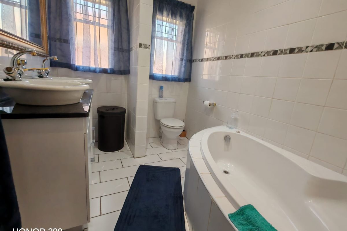 A functional bathroom featuring a built-in bathtub, a vanity with a vessel sink, and a toilet, finished with white wall and floor tiles.