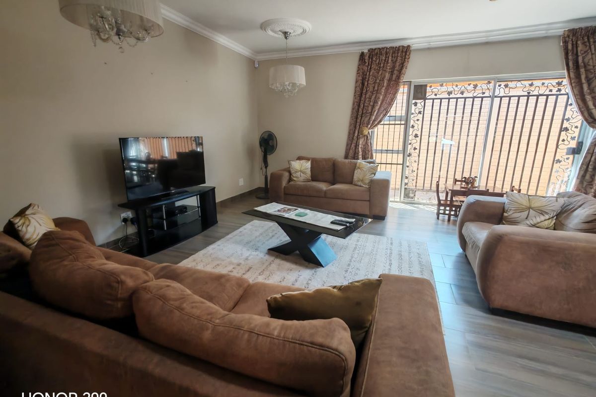 Spacious living room featuring tiled flooring, decorative ceiling roses, and a sliding glass door with integrated security gate leading to the exterior.