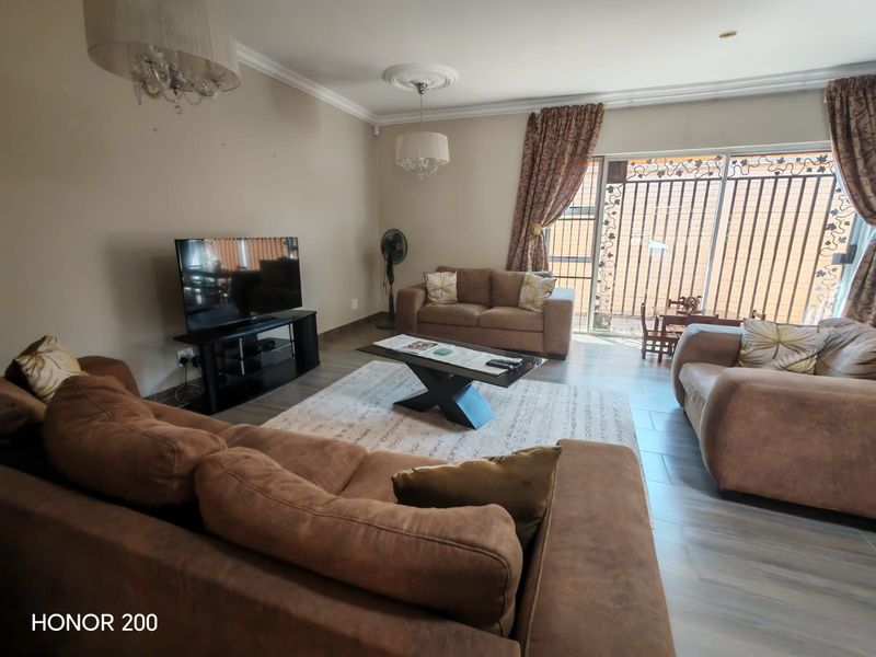 Spacious living room featuring tiled flooring, decorative ceiling roses, and a sliding glass door with integrated security gate leading to the exterior.