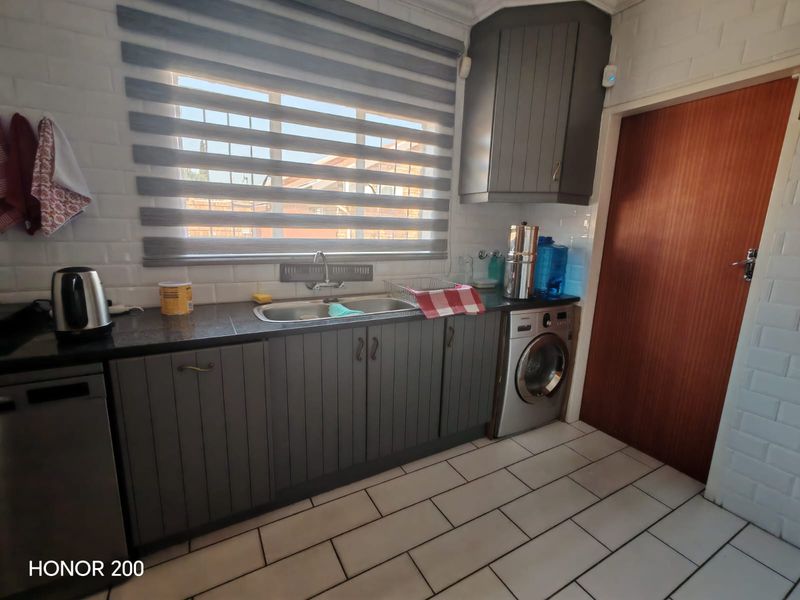 A functional kitchen featuring dark grey cabinetry, granite countertops, subway tile backsplash, and integrated laundry facilities with tiled flooring.