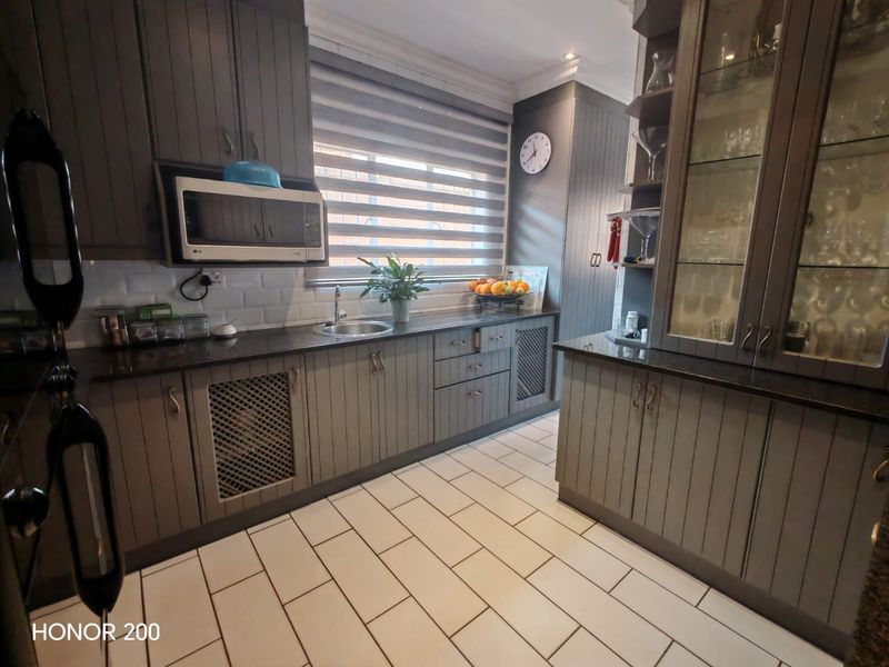 A well-maintained kitchen featuring dark grey cabinetry, granite countertops, built-in microwave, and glass-front display units with modern tiled flooring.