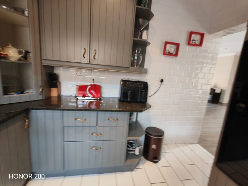 A functional kitchen area featuring grey shaker-style cabinetry, granite countertops, and a classic white subway tile backsplash with tiled flooring.
