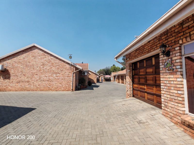 A view of the townhouse complex driveway featuring face-brick exterior walls, paved surfaces, and wooden garage doors.