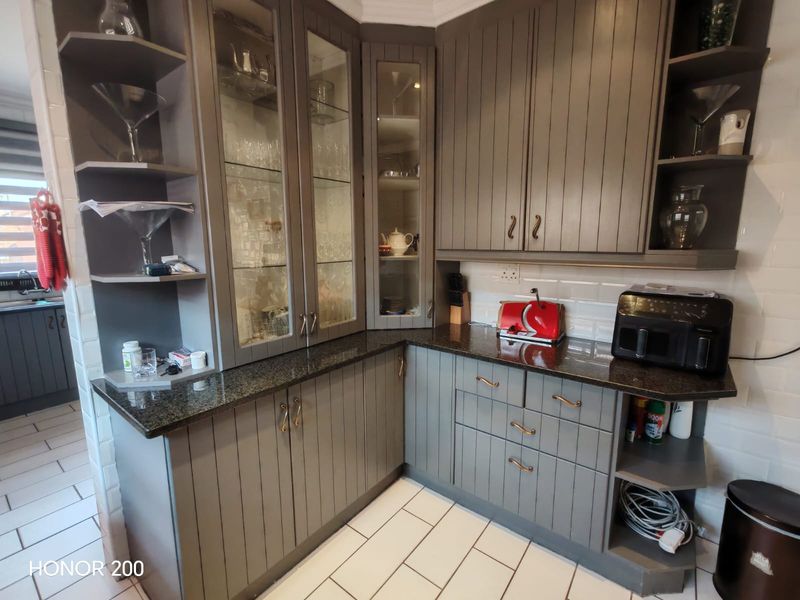 A well-maintained kitchen featuring grey cabinetry, granite countertops, glass-front display units, and a classic subway tile backsplash.