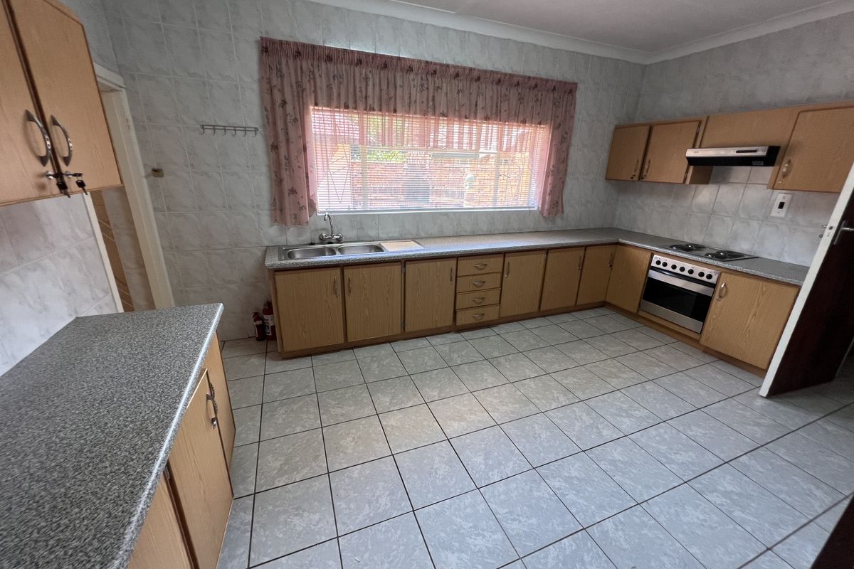 A functional kitchen featuring laminate cabinetry, tiled splashbacks, a double bowl sink, and built-in cooking appliances with ceramic floor tiles.
