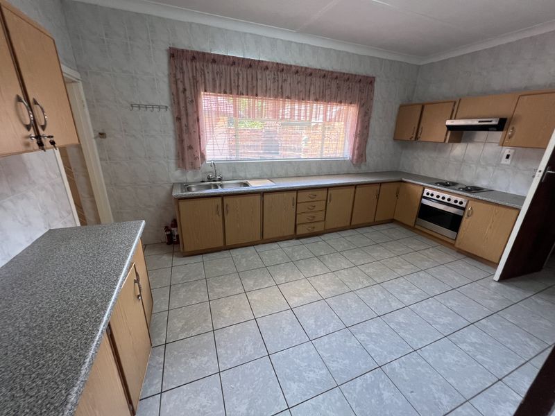 A functional kitchen featuring laminate cabinetry, tiled splashbacks, a double bowl sink, and built-in cooking appliances with ceramic floor tiles.