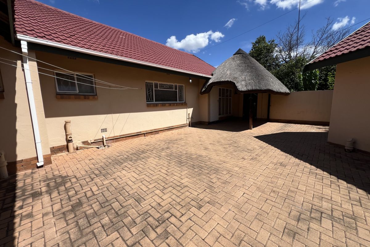 A paved rear courtyard featuring a traditional thatched lapa and access to the main house structure with tiled roofing.