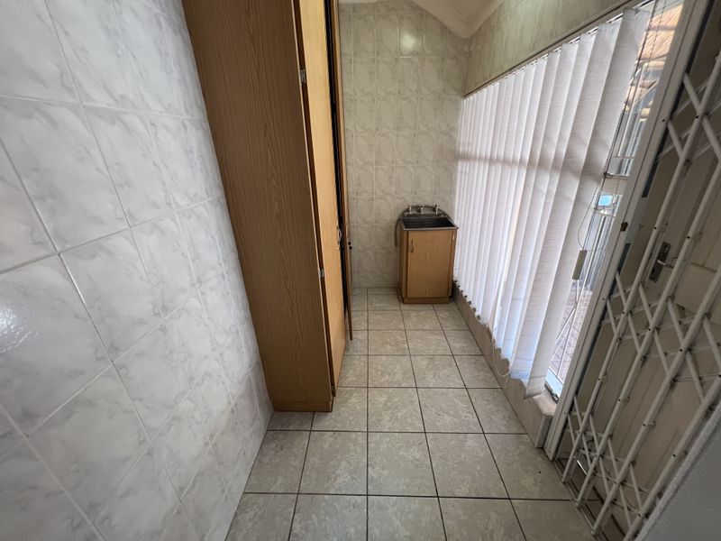 A functional laundry area featuring tiled walls and flooring, a built-in sink cabinet, and a security gate for added safety.