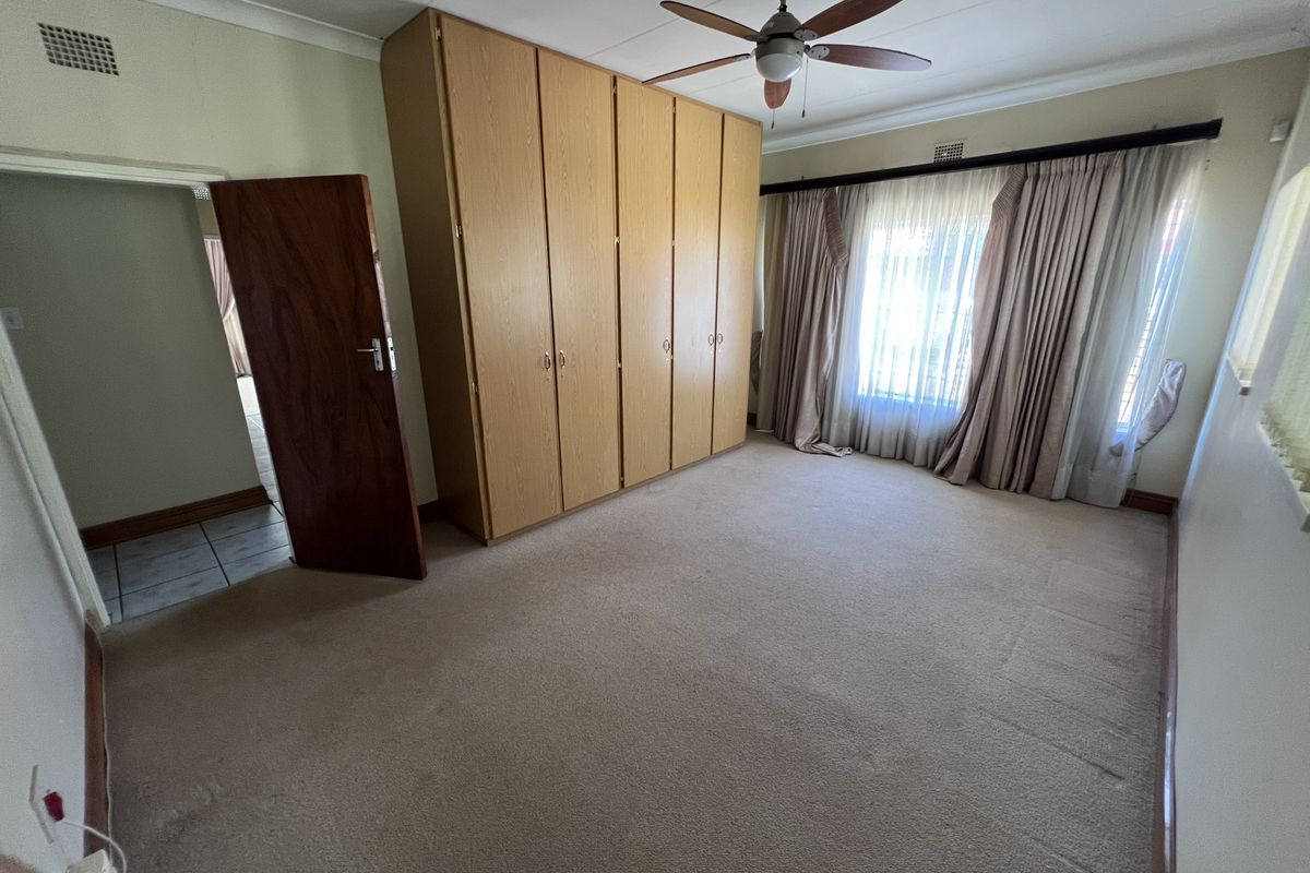 A spacious bedroom featuring neutral carpeting, built-in wooden cupboards, and a ceiling fan, offering a clean and functional space ready for personalization.