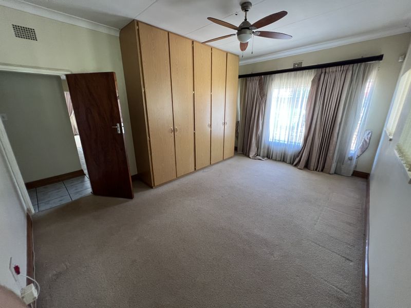 A spacious bedroom featuring neutral carpeting, built-in wooden cupboards, and a ceiling fan, offering a clean and functional space ready for personalization.