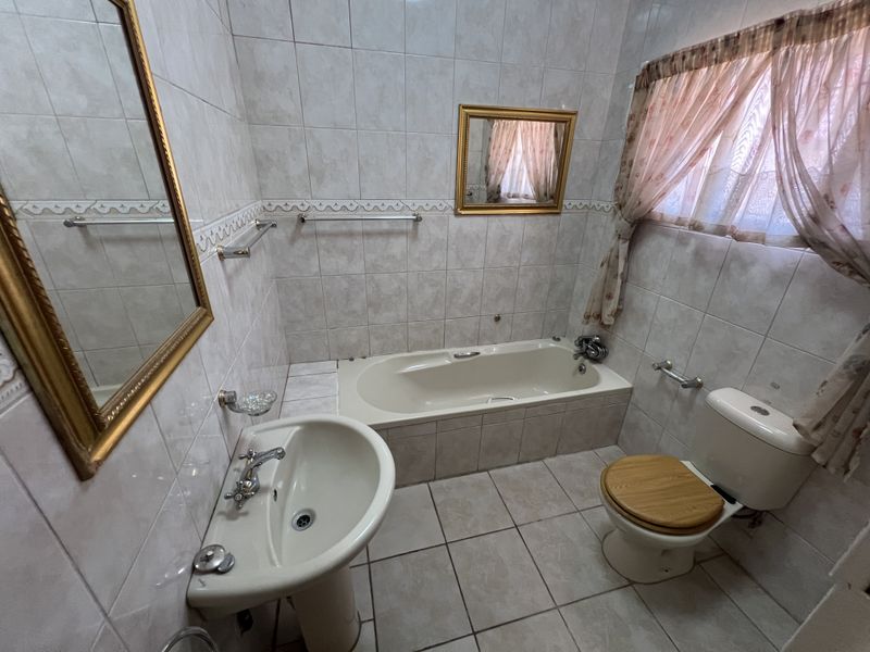 A functional bathroom featuring a pedestal basin, built-in bathtub, and toilet, finished with neutral ceramic wall and floor tiles.